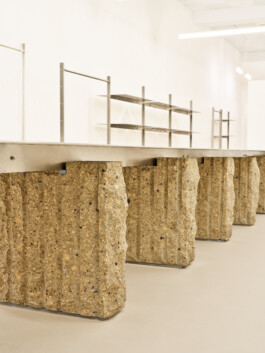 Detail: Textur des Natursteins und matte Reflexionen des gebürsteten Edelstahls am Tisch. Produkt-Fotografie